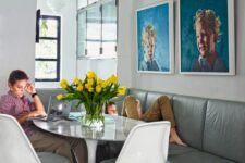 a cool dining space with a grey leather sofa, an oval table and grey Tulip chairs, a bright portrait gallery wall