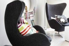 a cool nook with a letter bookshelf, black Egg chairs, colorful pillows, stacks of magazines and a coffee table