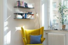 a cozy Scandinavian reading nook with a bookshelf, a mustard-colored Pape Bear chair, a rug and a lamp plus some plants