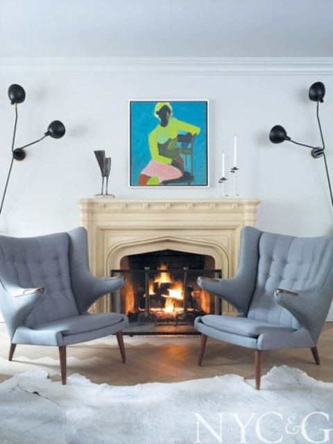 a cozy fireplace nook with a vintage fireplace, grey Papa Bear chairs, black sconces and a bold artwork is cool