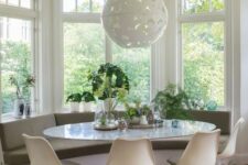 a cozy mid-century modern breakfast nook with a built-in windowsill bench, an oval table, olive green Tulip chairs, a pendant lamp