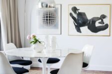 a fab dining space in neutrals with a round table, black Tulip chairs, some artworks, a metallic floor lamp and neutral textiles