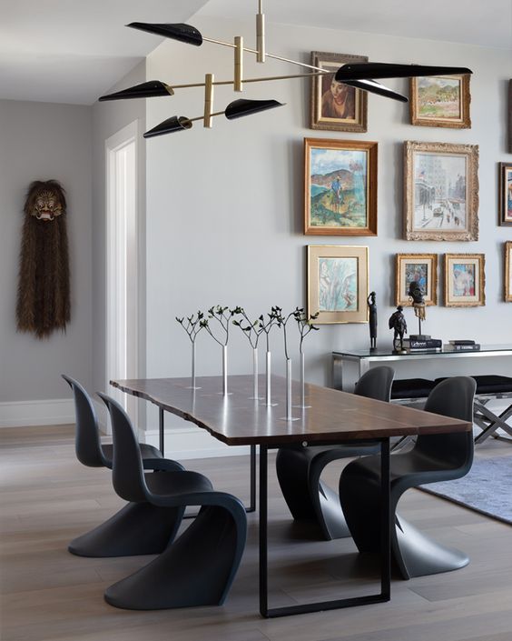 a gorgeous dining room with a stained table, black Panton chairs, a gallery wall, a bench and a black and gold chandelier