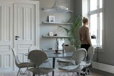 a grey Scandinavian dining space with open shelves, a round dining table, white Eames wire chairs with seat pads, a pendant lamp