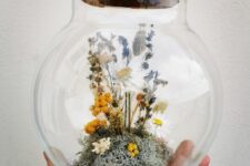 a large jar with a cork lid and some moss, dried neutral, yellow and blue blooms and some berries is a cool idea for quirky home decor