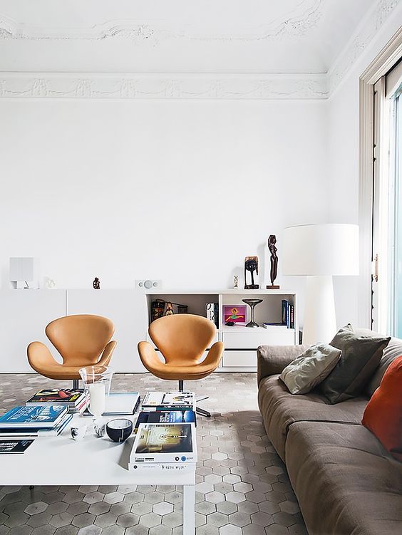 a lilvely living room with a taupe sofa and bold pillows, amber leather Swan chairs, a coffee table and a white storage unit