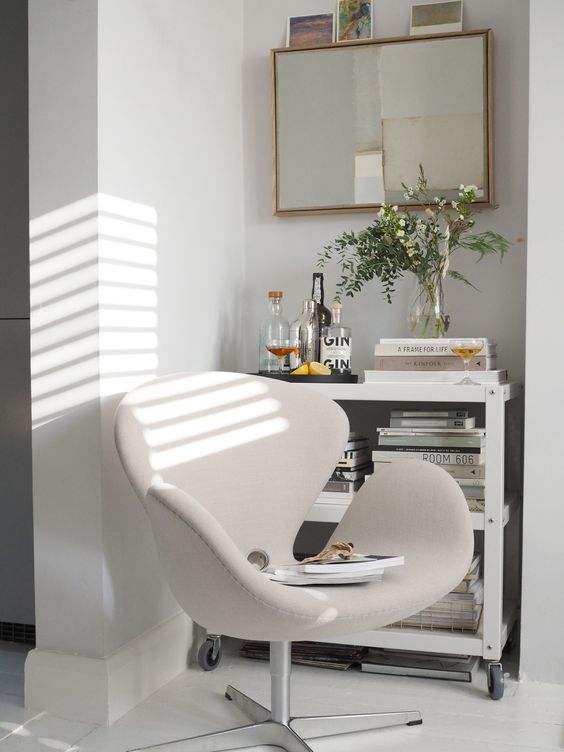 a lovely nook with a console table with a home bar, a mirror, some greenery and a creamy Swan chair with magazines