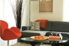 a mid-century modern living room with a grey sofa and printed pillows, an orange Swan chair, a glass table and a neutral rug