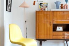 a mid-century modern space with a stained sideboard and some bright decor, a yellow Panton chair, some pastel lamps and decor