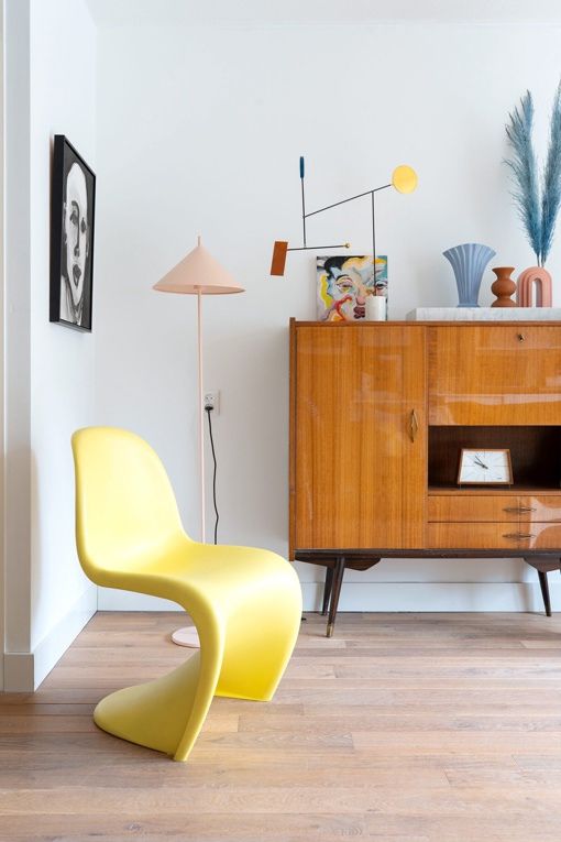 A mid century modern space with a stained sideboard and some bright decor, a yellow Panton chair, some pastel lamps and decor