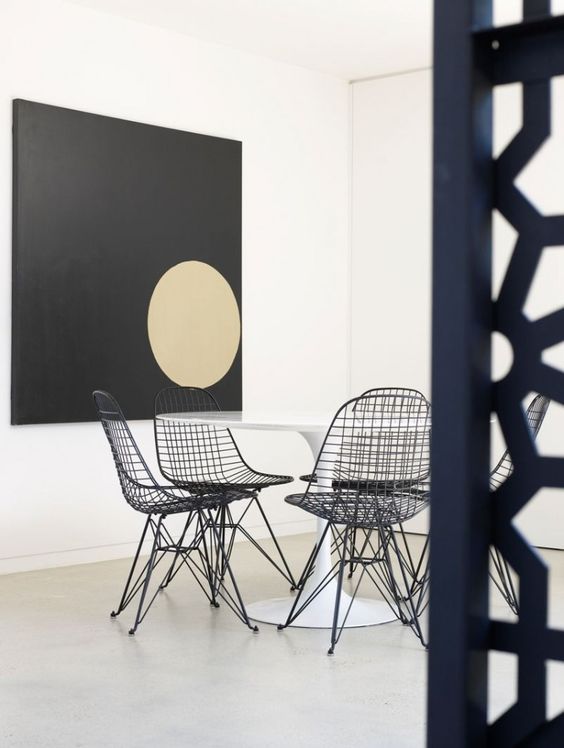 a minimalist dining space with a black artwork, a white round table, black Eames wire chairs is edgy and bold