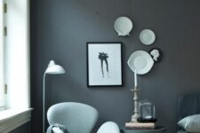 a monochromatic space with a grey accent wall, a black sofa and a pillow, a black side table, a light blue Swan chair and a footrest