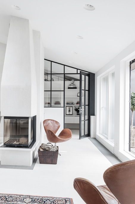 a monochromatic space with floor to ceiling windows, a fireplace, brown leather Swan chairs and a bit of firewood