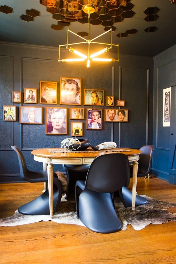 a moody dining room with graphite grey walls, a vintage stained table, black Panton chairs, a catchy chandelier and a gallery wall