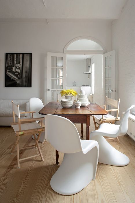 a neutral dining space with a stained table, mismatching chairs including Panton ones, a white sofa and artwork