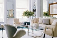 a neutral living room with a mirror wall, a neutral sofa with pillows, creamy chairs including a Swan one, a glass coffee table