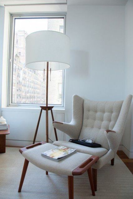 a neutral nook by the window with a creamy Papa Bear chair and a footrest, a floor lamp and a table with magazines