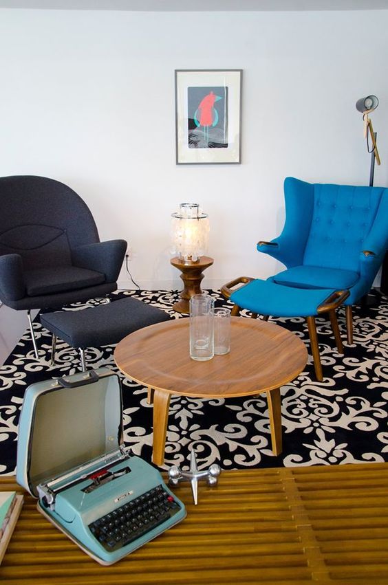 a retro space with a black Womb chair and a bold blue Papa Bear chair, a round table and a side one, a bold artwork