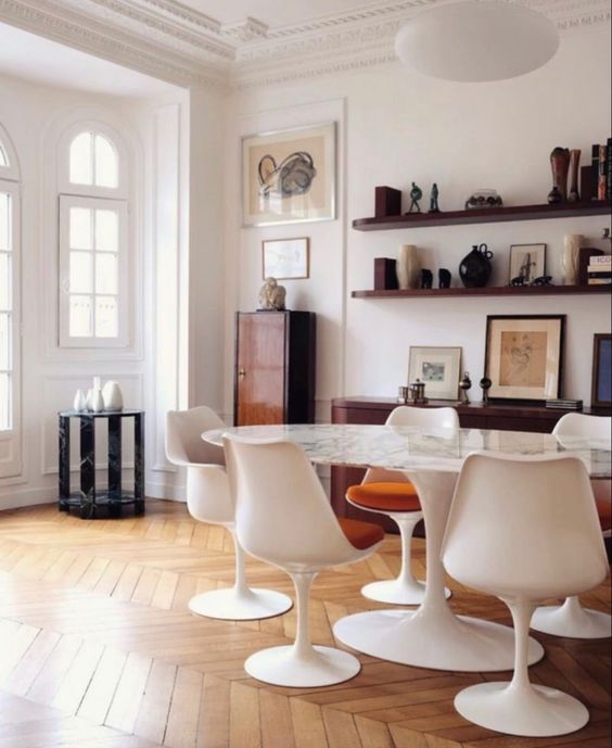 A sophisticated dining space with an oval table, rust colored chairs, stained shelves, a credenza, a cabinet and some decor and art