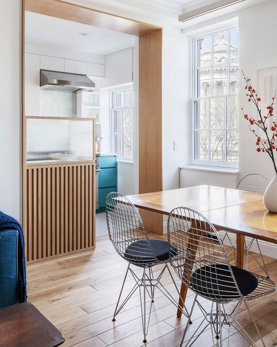 a stylish Scandinavian space with a kitchen flowing into a dining and living room, with a stained table and Eames wire chairs