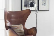 a stylish and catchy nook with a mini gallery wall, a brown leather Egg chair, a floor fan and a black floor lamp