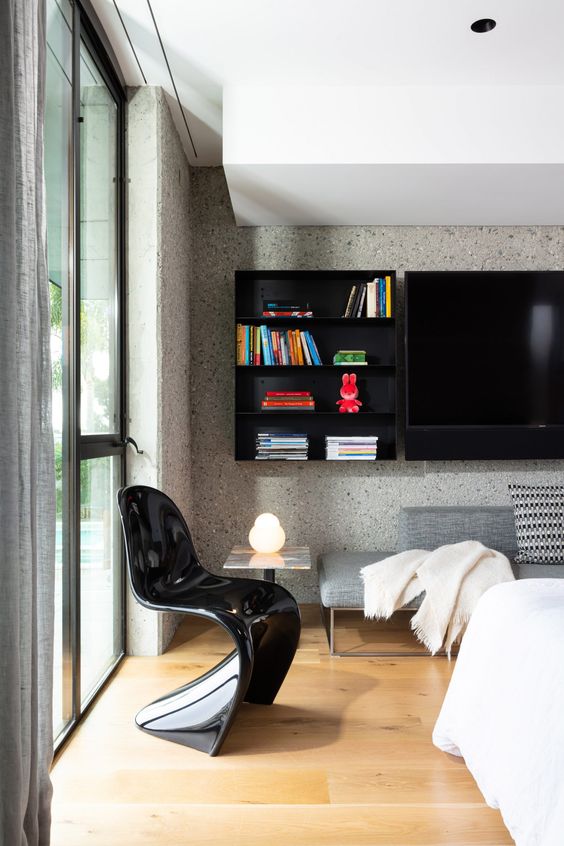 a stylish bedroom with terrazzo walls, a grey couch, a bed with neutral bedding, a black Panton chair, a black shelf and a TV