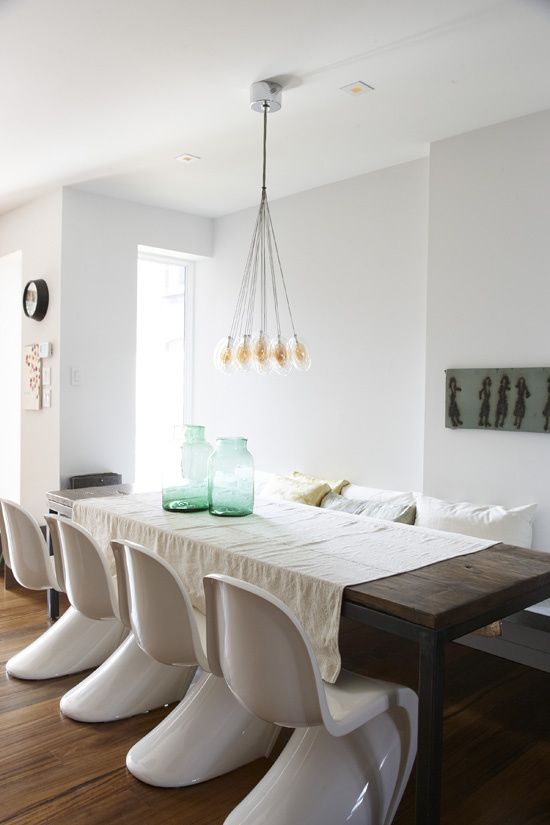 a stylish dining room with a stained table and bench, with white Pantone chairs, a chandelier and some decor