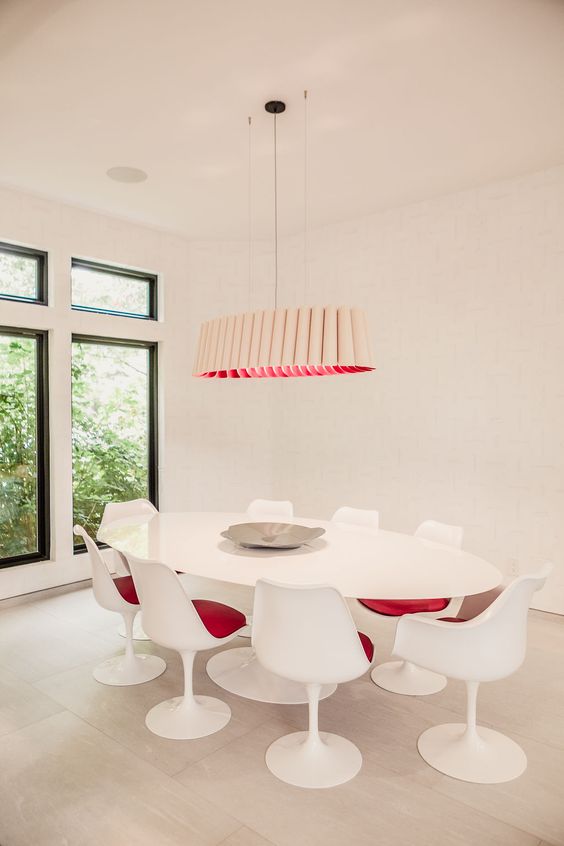 A stylish modern dining space in creamy shades, with a large oval table, pink Tulip chairs, a catchy tube like chandelier with pink inside
