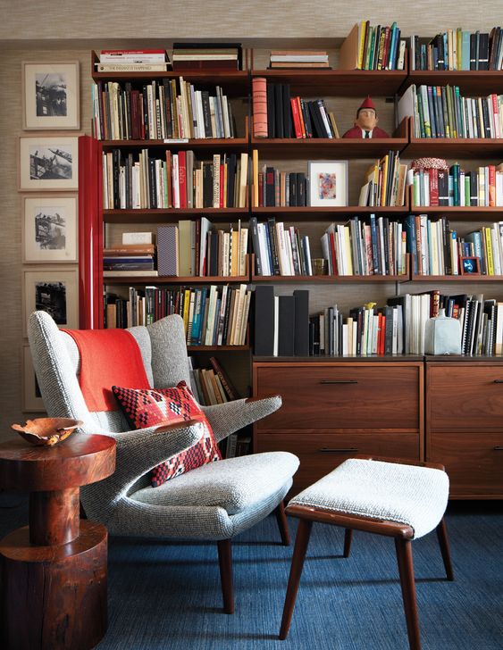 a stylish reading space with a large bookcase, a neutral Papa Bear chair with a footrest, a side table and art