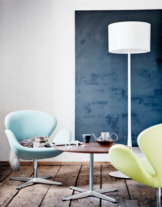 a stylish space with a navy accent wall, a light blue and neon yellow Swan chairs, a coffee table and a floor lamp is cool