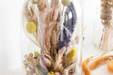 a tall cloche with pink and purple dried grasses, billy balls, berries and some lights inside is a pretty and bright decoration