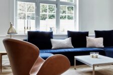an airy Scandinavian living room with a navy sofa and pillows, an amber Swan chair, a table lamp and a coffee table