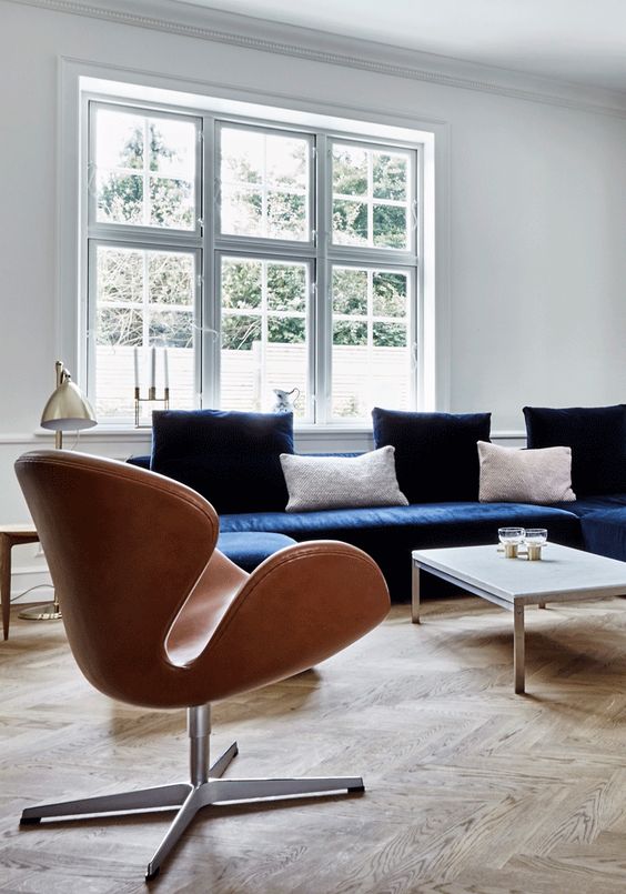 an airy Scandinavian living room with a navy sofa and pillows, an amber Swan chair, a table lamp and a coffee table