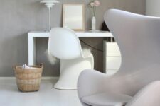 an airy Scandinavian space with a concrete accent wall, a white desk, a white sculptural chair, a grey Egg chair, a lamp and a basket