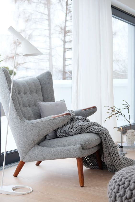 an airy Scandinavian space with a grey Papa Bear chair with a pillow and a blanket, a white floor lamp and a candle