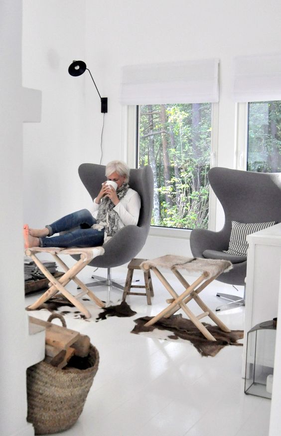 an airy Scandinavian space with grey Egg chairs, wooden footrests and animal skin rugs and a black lamp