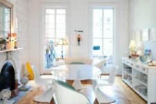 an eclectic dining room with a fireplace, a white storage unit, a white oval table, white Panton chairs, s creamy sofa and some decor