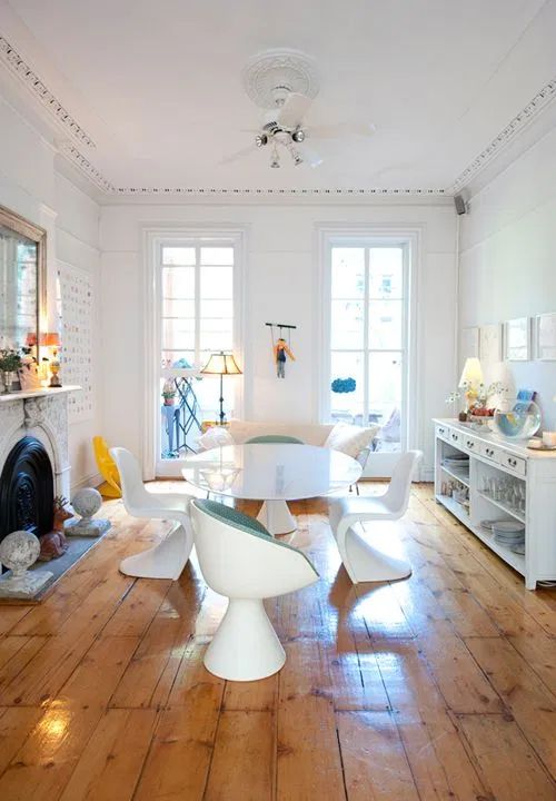 an eclectic dining room with a fireplace, a white storage unit, a white oval table, white Panton chairs, s creamy sofa and some decor