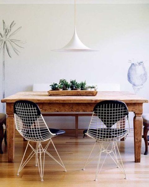 an eclectic dining room with a stained table, white Eames wire chairs, potted greenery, a white pendant lamp and some decor
