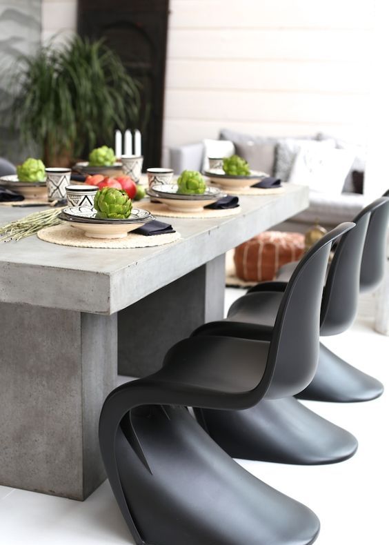 an outdoor dining space with a concrete table, black Panton chairs, a sofa and a leather pouf is cool and lovely