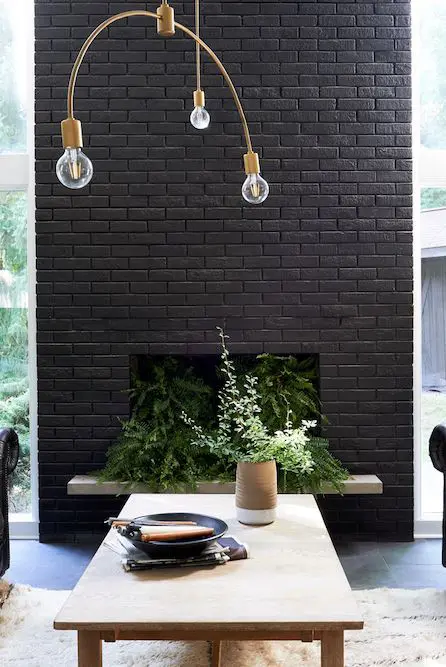 a beautiful and refined black brick fireplace filled with greenery and with a gold chandelier over it