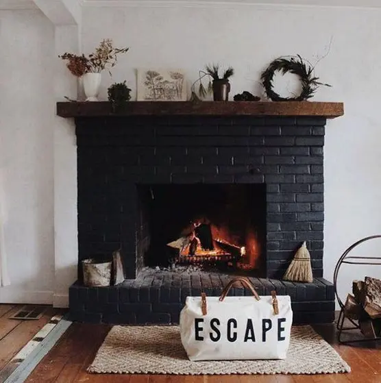 a black brick fireplace with a wooden mantel with various plants and some accessories plus a firewood stand next to it