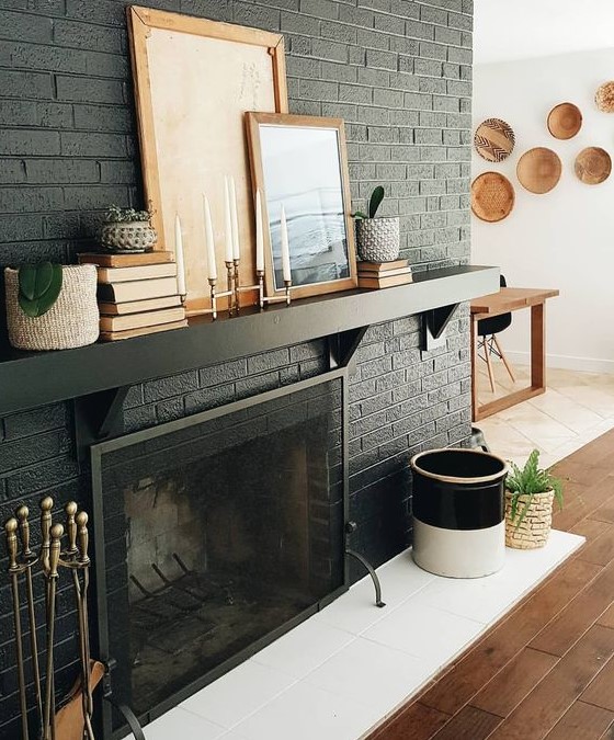 a black brick fireplace with white tiles in front of it, a black mantel with books and artworks for stylish monochromatic decor