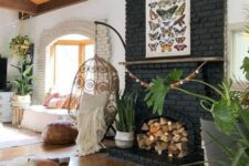 07 a boho living room with a black brick fireplace filled with firewood and plants in baskets plus a butterfly poster on it