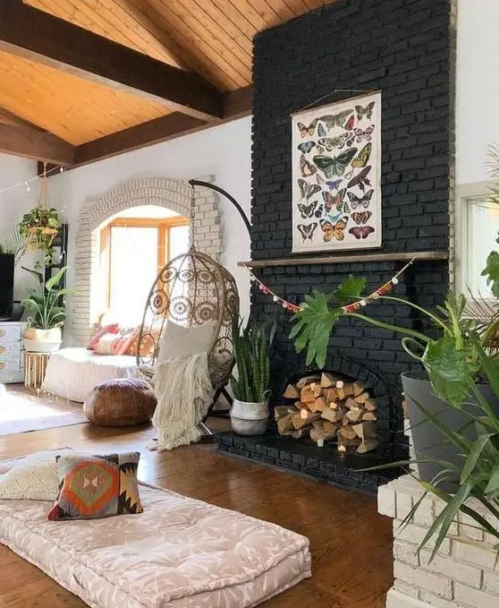 a boho living room with a black brick fireplace filled with firewood and plants in baskets plus a butterfly poster on it