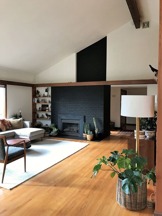 A mid century modern living room with a black brick fireplace, built in shelves, a neutral sofa, chairs and potted plants