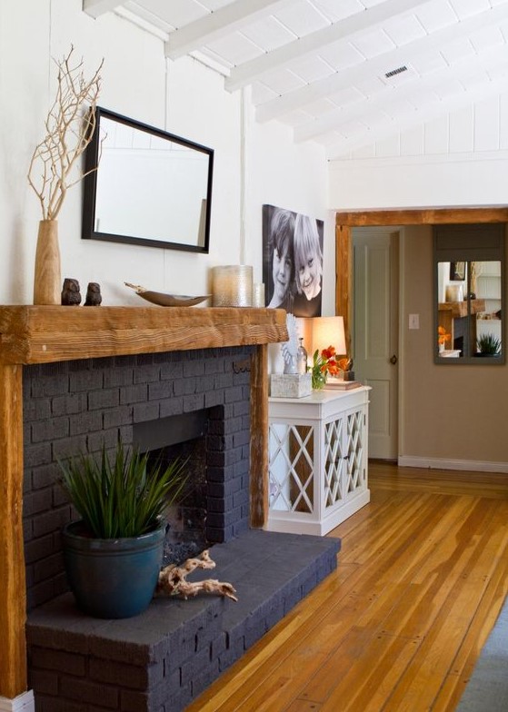 a stylish black brick fireplace with a rough wood mantel and frame, with some decor is a bold decor feature