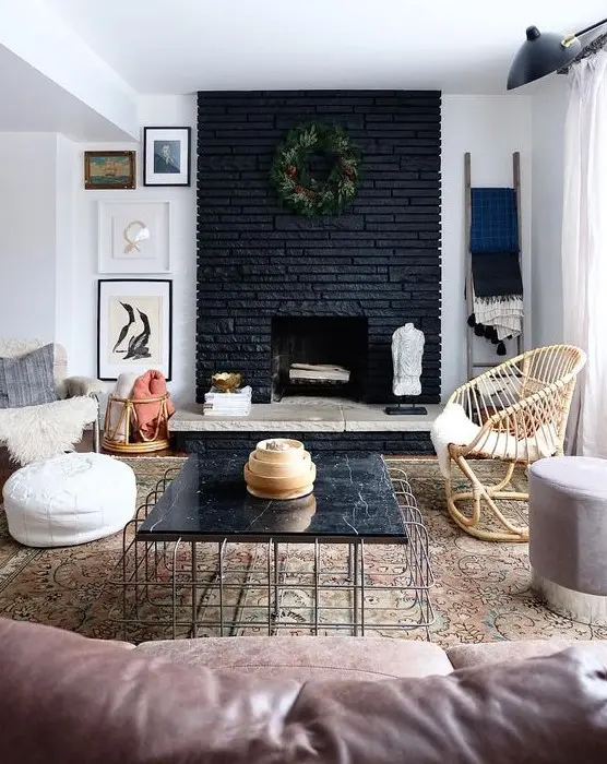 an eclectic living room with a black brick fireplace, stone and a greenery wreath and a black marble table that echoes with it
