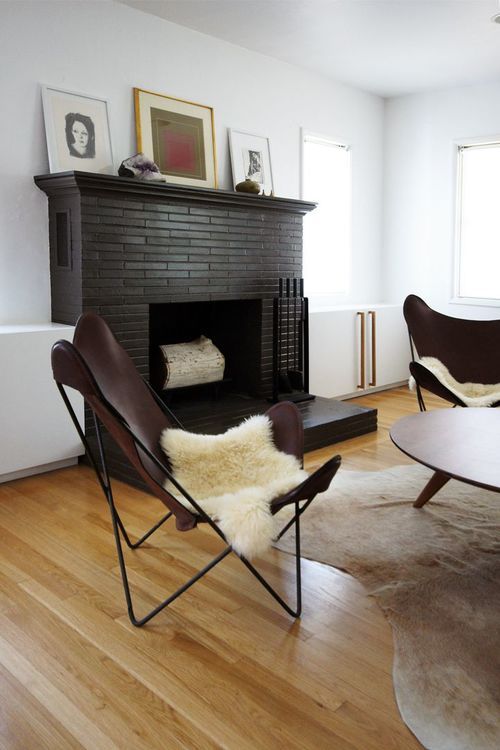 An elegant mid century modern living room with a black painted brick fireplace, leather butterfly chairs, a low coffee table and animal skins