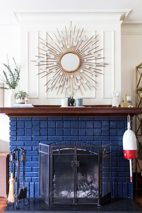 a beautiful and chic navy brick fireplace with a metal screen, a stained mantel with decor, a sunburst mirror over the mantel